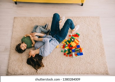 Overhead View Of Smiling Mom And Son Lying On Carpet With Toy Blocks