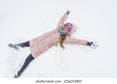 Overhead view of smiling woman lying on snow and making snow angel figure with hands and legs. High quality photo - Shutterstock ID 2256252807