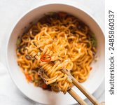 Overhead view of Spicy instant noodles with slices of green and red chili, spicy ramen noodles on chopsticks in a white ceramic bowl