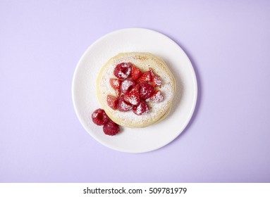 Overhead view of a stack of berry covered pancakes on a pastel purple background