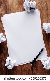 Overhead View Of A Stack Of Blank White Sheets Of Paper Surrounded With Crumpled Remnants Screwed Up In Frustration On A Wooden Desk