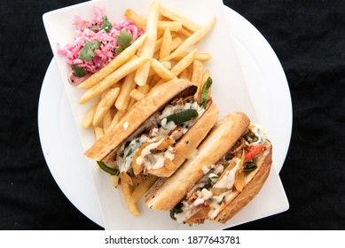 Overhead View Of Stacked And Layered Cheese Steak Sandwich Cut In Half To Show Cross Section Of Ingredients Served With French Fries.