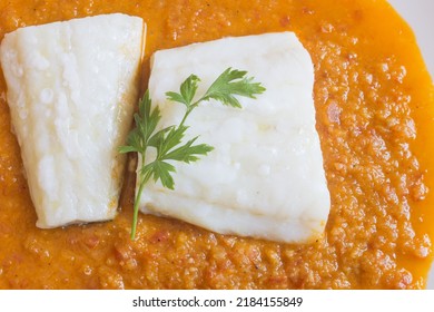 Overhead View Of A Steamed Cod Fillet With Tomato Sauce And A Sprig Of Fresh Parsley On A White Plate. White Fish And Close Up.