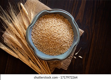 Overhead View Of Steel Cut Oats In A Small Bowl On A Wooden Surface With An Accent Of Burlap And Dried Oat Stems