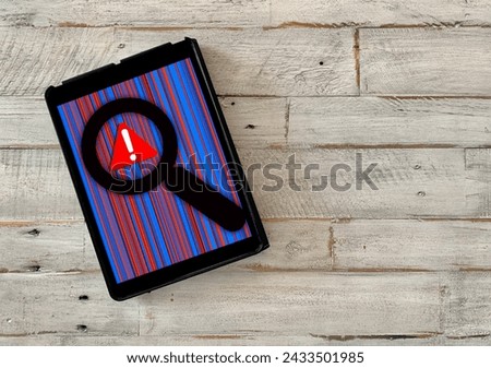 Overhead view of tablet with data patterns and warning sign viewed with magnifying glass for safer internet concept on wooden workspace surface.	