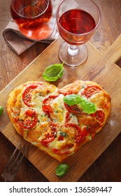 Overhead View Of A Tasty Cheese And Tomato Vegetarian Heart Shaped Pizza Served On A Wooden Board With A Glass Of Red Wine