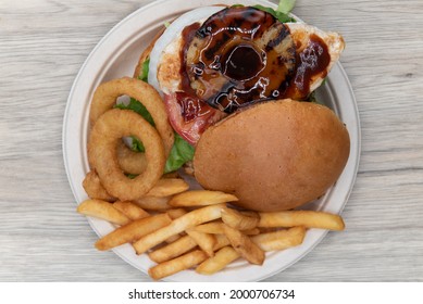 Overhead View Of Teriaki Chicken Sandwich Glazed With Sweet Sauce And Pineapple Served With Onion Rings And French Fries.