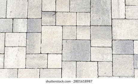 An overhead view of a textured interlocking stone paver walkway featuring an ashlar pattern of light grey beige and white masonry blocks filling the entire frame