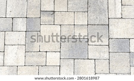 An overhead view of a textured interlocking stone paver walkway featuring an ashlar pattern of light grey beige and white masonry blocks filling the entire frame
