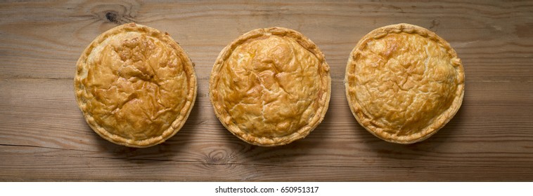 Overhead View Of Three Cooked Round Meat Pies On A Wooden Countertop