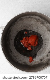 Overhead view of tomato paste being fried in a cast aluminum pot, top view of tomato paste being fried to make nigerian jollof rice, process of making jollof rice
