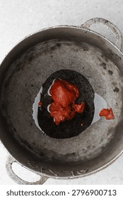 Overhead view of tomato paste being fried in a cast aluminum pot, top view of tomato paste being fried to make nigerian jollof rice, process of making jollof rice