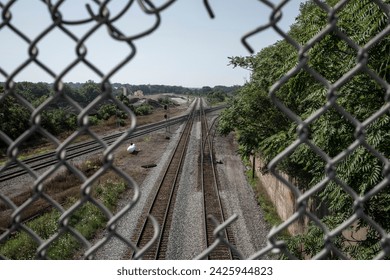 Overhead view of train tracks through hole in chain link fence