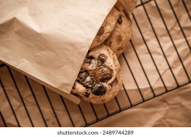 An overhead view of two freshly-baked chocolate chip cookies placed on a metal wire cooling rack underneath a brown paper bag - Powered by Shutterstock