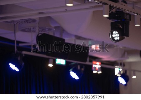 Overhead view of various stage lighting and audio equipment, including spotlights, moving head fixtures, and sound speakers, mounted to a ceiling structure for an event