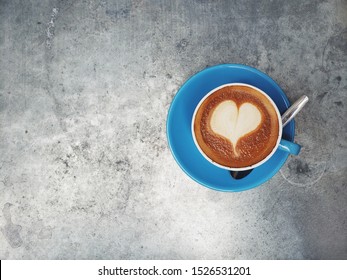 Overhead View Of Vegan Oat Milk Latte With Heart Shape In Foam Served In Blue Ceramic Mug With Spoon On Silver Metal Background Surface / Coffee Love Concept