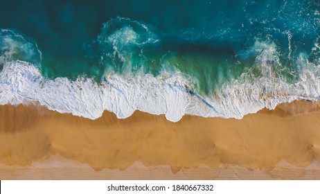 Overhead view of waves hitting the yellow sand and blue ocean