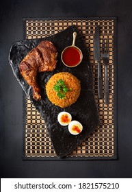 Overhead View Of A West African Entree Of Jollof Rice, Chicken, Boiled Egg And Shito Sauce On A Dark Surface