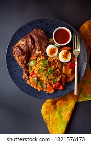 Overhead View Of A West African Entree Of Chicken, Jollof Rice, Roasted Vegetables, Boiled Egg And Shito Sauce