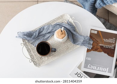 Overhead view of a white coffee table with a cup of coffee, sugar bowl, and travel magazine for a relaxing morning