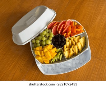 Overhead view of white divided serving tray with ice compartment filled with assorted fresh sliced fruits on wooden table