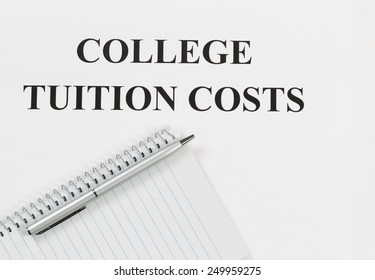 Overhead View Of White Paper With Wording Of College Tuition Cost Along With Silver Pen And Notebook. 