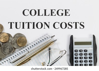 Overhead View Of White Paper With Wording Of College Tuition Costs Along With Silver And Gold Pens, Calculator, Coin Money, Reading Glasses And Notebook. 