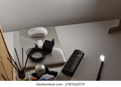 Overhead view white wireless computer mouse on closed silver laptop with power adapter on light desk surface