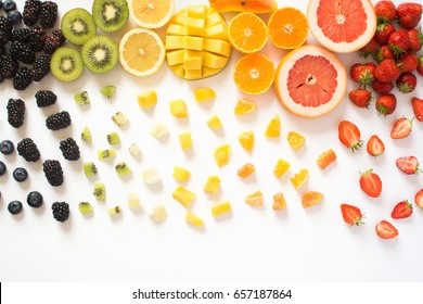 Overhead View Of Whole Fruits And Cut Slices In The Rows, Red, Orange, Yellow, Green Fruits With Cut Pieces On The White Background, Grapefruit, Mango, Strawberries, Orange, Lemon, Kiwi