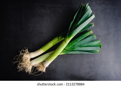 Overhead View of Whole Leeks on a Dark Background: Three leeks with leaves and roots on a stone countertop