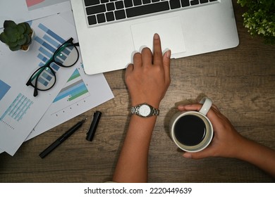 Overhead View Of Woman Hand Holding Coffee Cup And Using Laptop On Wooden Office Desk