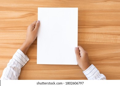 Overhead View Of Woman Holding Blank Paper Sheet A4 Size Or Letter Paper On Wooden Desk Background, Copy Space