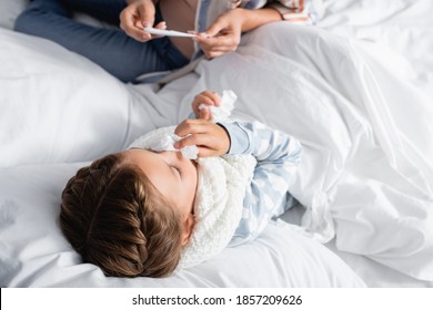 Overhead View Of Woman Looking At Thermometer Near Sick Daughter Lying In Bed With Paper Napkin