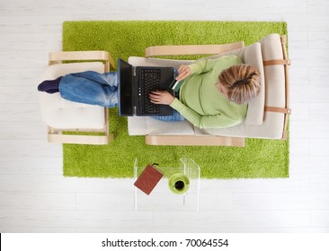 Overhead View Of Woman Sitting In Armchair Shopping From Home With Computer And Credit Card.?