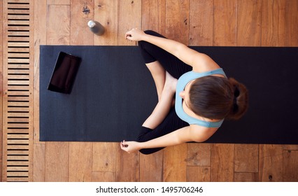 Overhead View Of Woman Sitting On Exercise Mat Using Digital Tablet