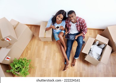 overhead view of young black african couple with moving boxes in new apartment using modern tablet computer technology