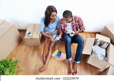 overhead view of young black african couple with moving boxes in new apartment choosing colour of paint for walls