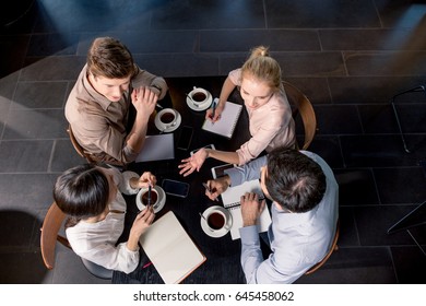 Overhead View Of Young Businesspeople Discussing Project At Table With Cups Of Coffee, Business Lunch Concept