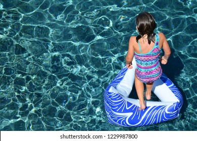 Overhead View Of Young Girl Jumping Through Inner Tube Into Sparkling Water Of A Swimming Pool.