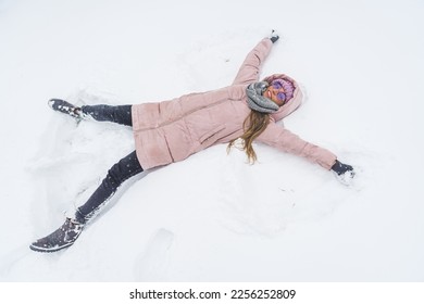 Overhead view of young smiling woman with pink winter coat on making a snow angel. High quality photo - Shutterstock ID 2256252809