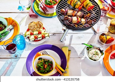 Overhead Well Laid summer table with colorful dish and plates and brazier on white background with vegan bbq skewers