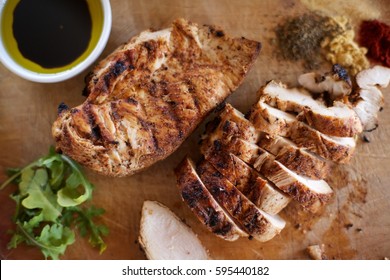 Overhead Window Light Food Prep Scene Of Whole And Sliced Seasoned Barbecued Chicken Breast With Arugula Greens And Pile Of Colorful Ground Spices And Dish Of Balsamic Olive Oil On Wood Cutting Board