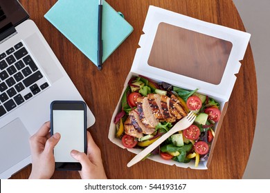 Overhead of work station, laptop computer with hands and takeout salad