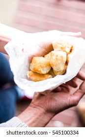 Overhead Of Young Woman Holding Fresh Donut Holes In Wax Paper Bag Over Brick Background.