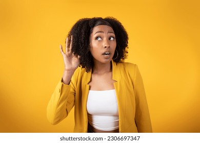 Overhearing, gossips and interesting news. Curious black curly lady listening secrets eavesdropping holding hand near ear posing over yellow studio background - Powered by Shutterstock