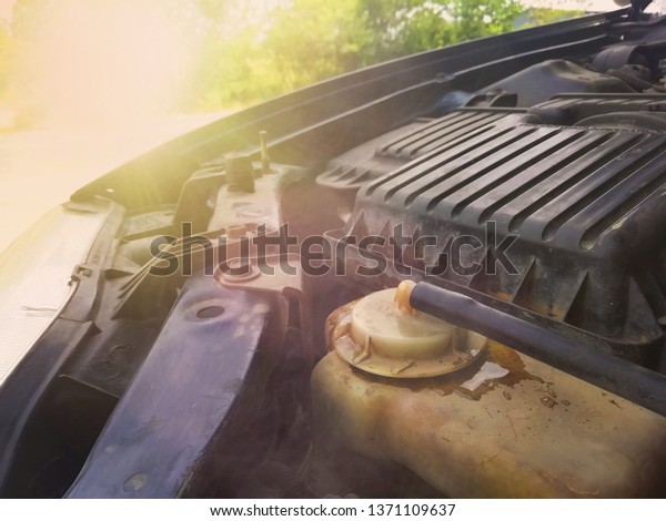 Overheat car is radiator reserve tank with heat or hot\
water splash out of the tank of old car  next to the radiator cap\
and smoke steam in tank with sunlight  needs to repair coolant\
broken accident 