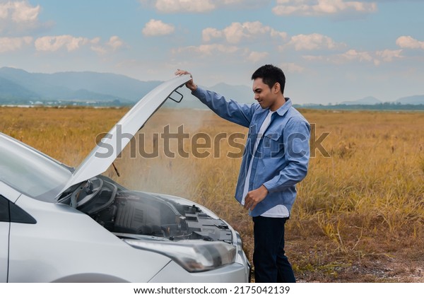 Overheated car and engine broke with breakdown\
radiator steam and hot oil smoke from under the hood. Asian young\
man auto driver standing open car hood on outdoors. Automobile\
motor problem\
concept.