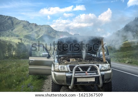 overheated car in the field, bright sunlight, steam under the hood. smoking engine in SUV car. Smoke coming out from overheat engine. Waiting car tow service. Mountain Altai, Russia