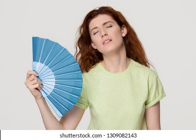 Overheated Redhead Woman Sweating Feel Uncomfortable Suffer From Heat Stroke Perspiration Problem, Tired Sweaty Lady Waving Fan Cooling In Hot Summer Weather Isolated On White Grey Studio Background