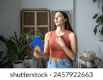 Overheated tired woman standing in room at hot summer weather day feels discomfort, suffers from heat waving blue hand fan to cool. Exhausted sweating dwelling female without air conditioner at home. 